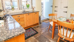 A kitchen with wooden cabinets, a granite countertop, a sink, and a dining area with a table and chairs. - Rose Cottage (Skipton)