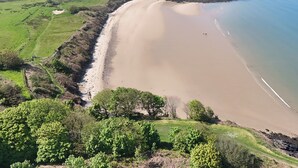 Vista aérea de un paisaje costero con una playa arenosa, campos verdes y una masa de agua.