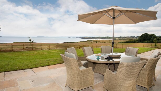 Un patio al aire libre con mobiliario de mimbre y una mesa, con vistas a una playa y al mar.