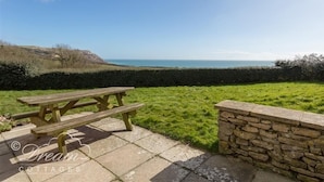 Une table de pique-nique et un muret de pierre se trouvent dans un espace verdoyant, avec vue sur la mer.