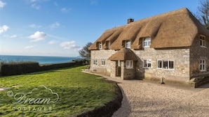 Une charmante maison en pierre avec un toit de chaume, une allée en gravier et une vue sur la mer.