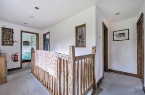 A hallway with a wooden bench, a fire extinguisher, and a bed with a patterned bedspread.