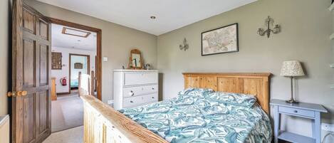 A bedroom with a wooden bed, a dresser, a nightstand, and a wall-mounted lamp.