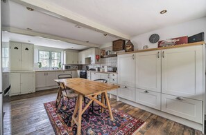 A kitchen with white cabinets, a wooden table, and a patterned rug.