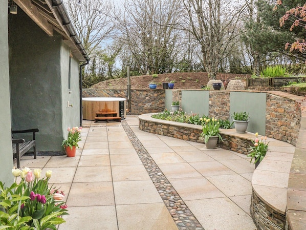 A patio area with a stone wall, potted plants, and a wooden bench. - Spring Park Farmhouse (Launceston)