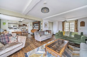 A spacious living room with a sofa, a coffee table, and a dining area with chairs and a table. - Spring Park Farmhouse (Launceston)