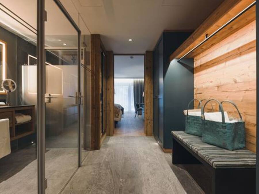 A hallway with a bench, wooden wall paneling, and a glass door leading to a room with a mirror and a shelf.