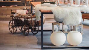 A cozy interior with a wooden table, white fur throw, and a vintage cart. Shelves in the background hold decorative items and candles. - Alpenhotel Montafon & SPA (Schruns)