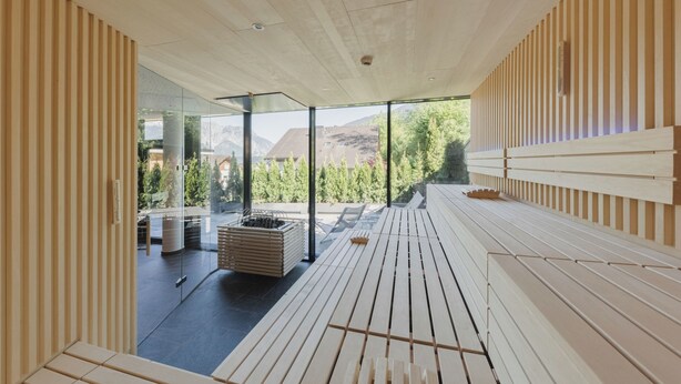 A modern interior with a wooden slatted wall, a bench, and a view of the outdoors. - Alpenhotel Montafon & SPA (Schruns)