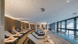 A modern indoor pool area with sun loungers and a view of the city. - Alpenhotel Montafon & SPA (Schruns)