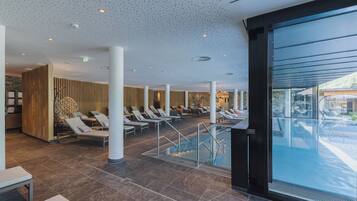 A modern indoor pool area with lounge chairs, a glass staircase, and a view of the outdoors.