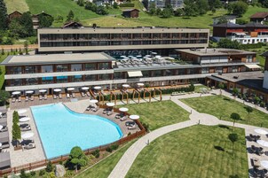 Un hotel moderno con piscina en la azotea, mobiliario exterior y un césped bien cuidado.