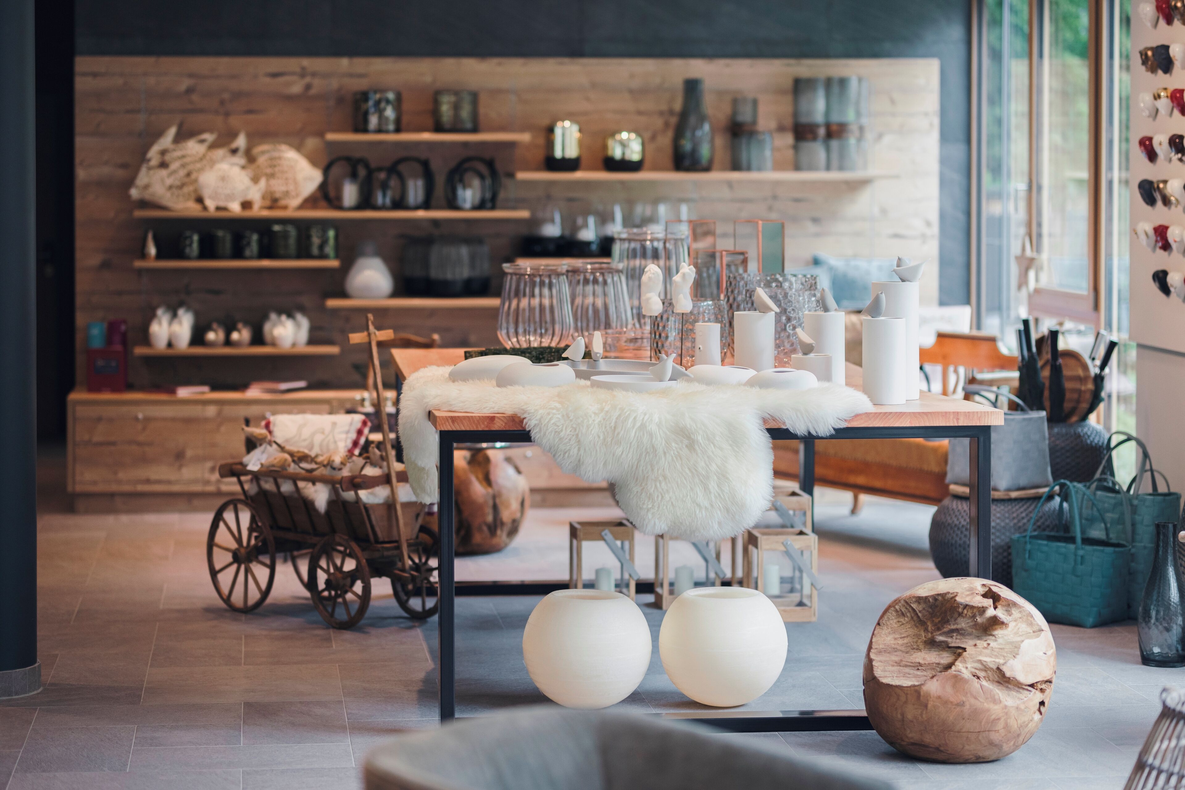 Un intérieur chaleureux avec une table en bois, des bougies blanches et une chaise rustique. Des étagères en arrière-plan présentent divers objets décoratifs.