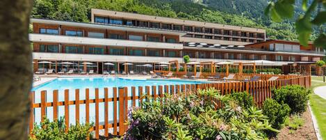 Een hotel met een zwembad, terras en een bergachtige achtergrond.