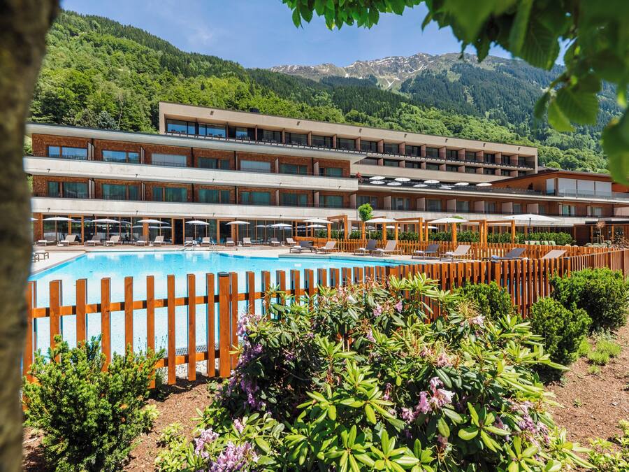 Een hotel met een zwembad, terras en een bergachtige achtergrond.