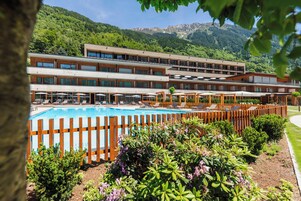 Un hotel con piscina, mobiliario exterior y montañas al fondo.