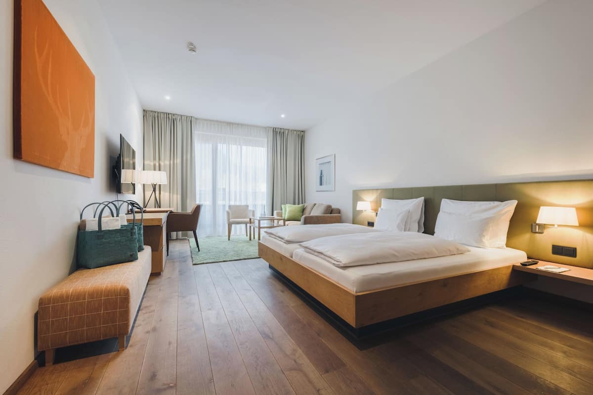 A hotel room with a large bed, a desk, a chair, and a bench.