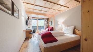 Ein Schlafzimmer mit Holzboden, einem Bett mit weißer und roter Bettwäsche, einem Schreibtisch mit Stuhl und einem Fenster mit Vorhängen.