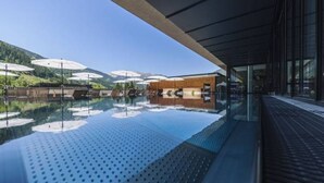 An infinity pool with a clear view of the mountains, a wooden deck, and umbrellas. - Alpenhotel Montafon & SPA (Schruns)
