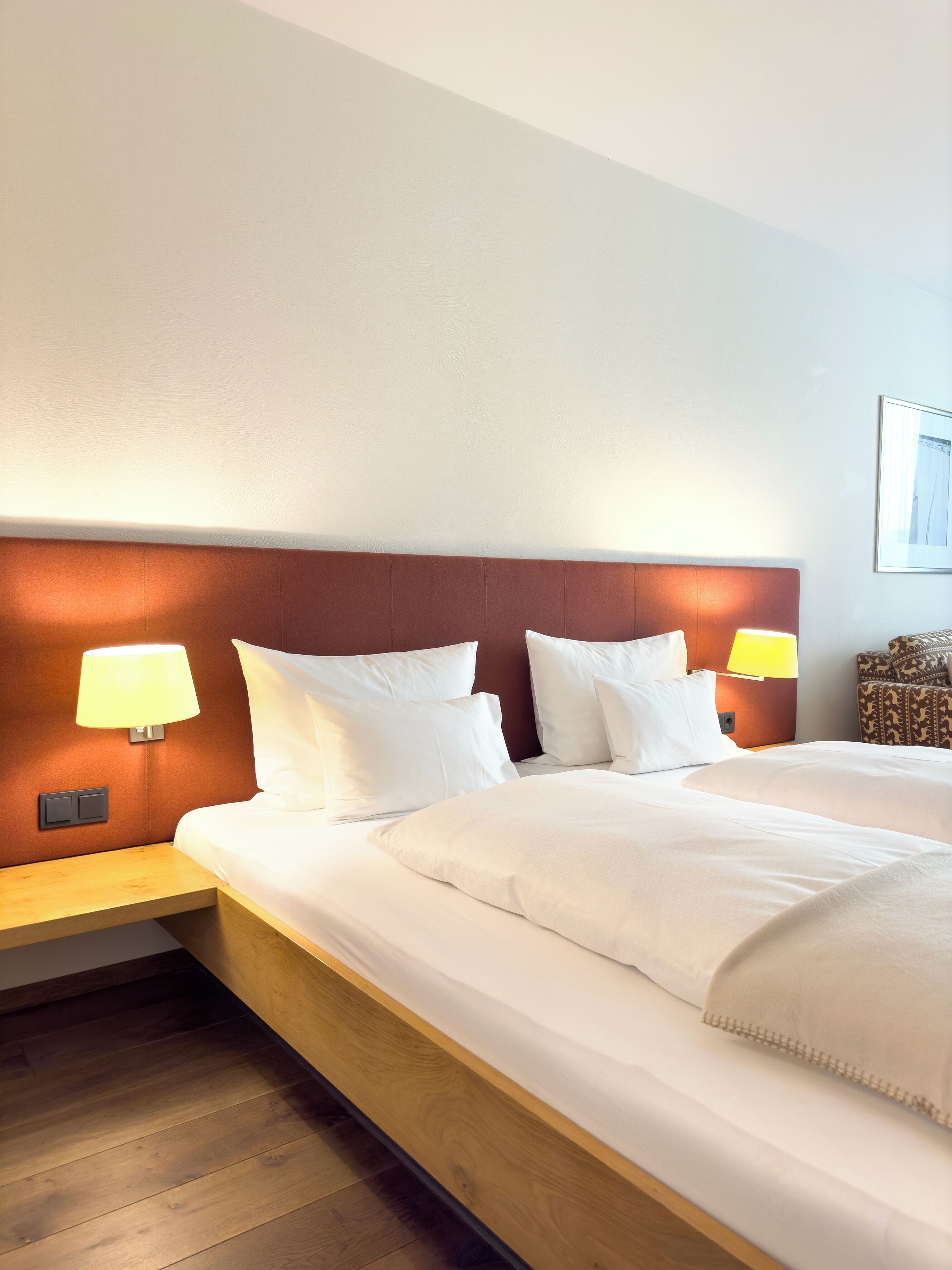 A hotel room with a large bed, two bedside lamps, a wooden nightstand, and a patterned armchair.