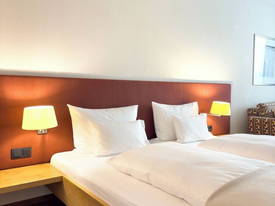 Ein Hotelzimmer mit einem großen Bett, zwei Nachttischlampen, einem Holznachttisch und einem gemusterten Sessel.