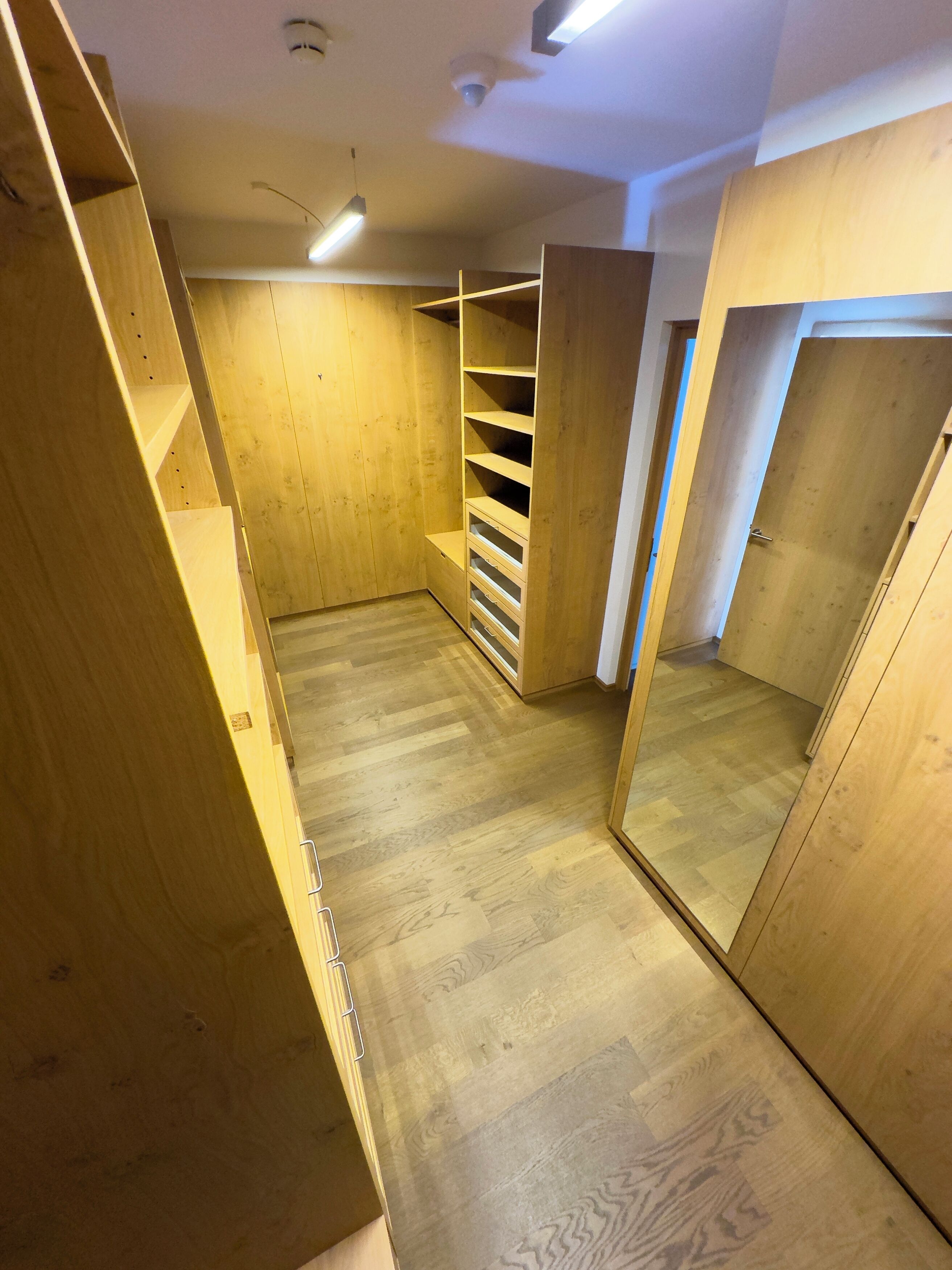 Un vestidor con estantes de madera y un espejo en la puerta.