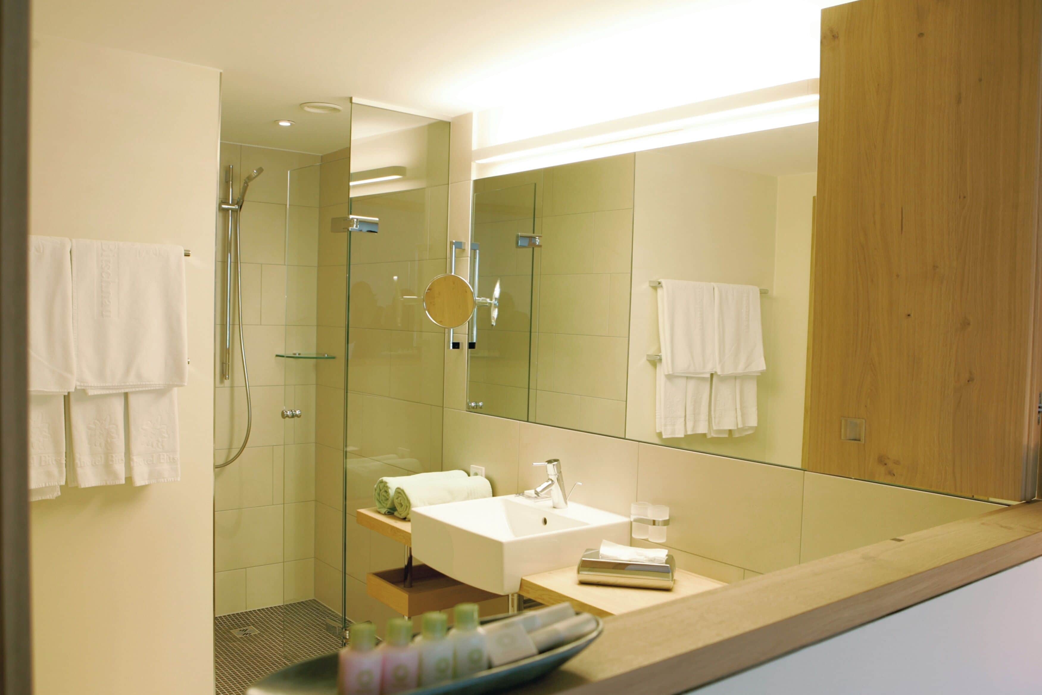Ein modernes Badezimmer mit einer Duschkabine aus Glas, einem weißen Waschbecken und einem großen Spiegel.