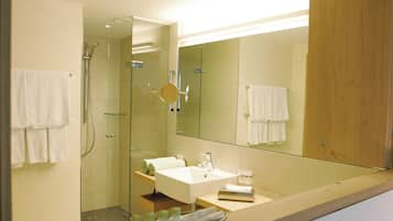 Ein modernes Badezimmer mit einer Duschkabine aus Glas, einem weißen Waschbecken und einem großen Spiegel.