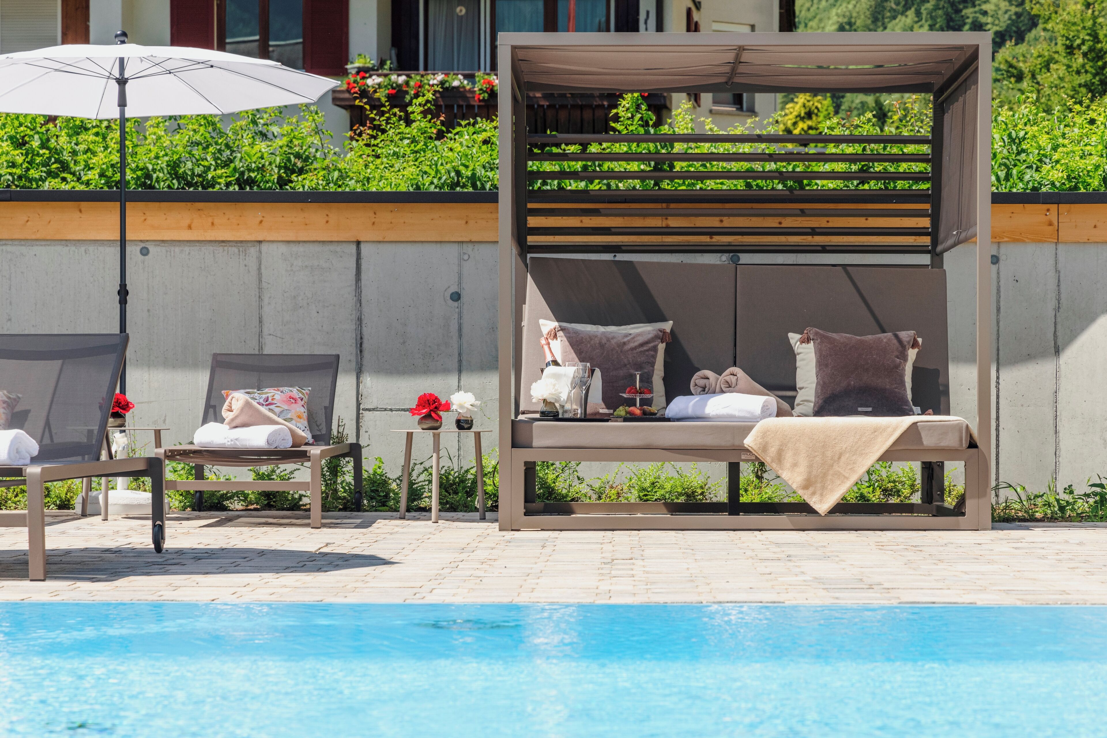Area piscina con lettini, una pergola e un tavolino con un vaso di fiori.