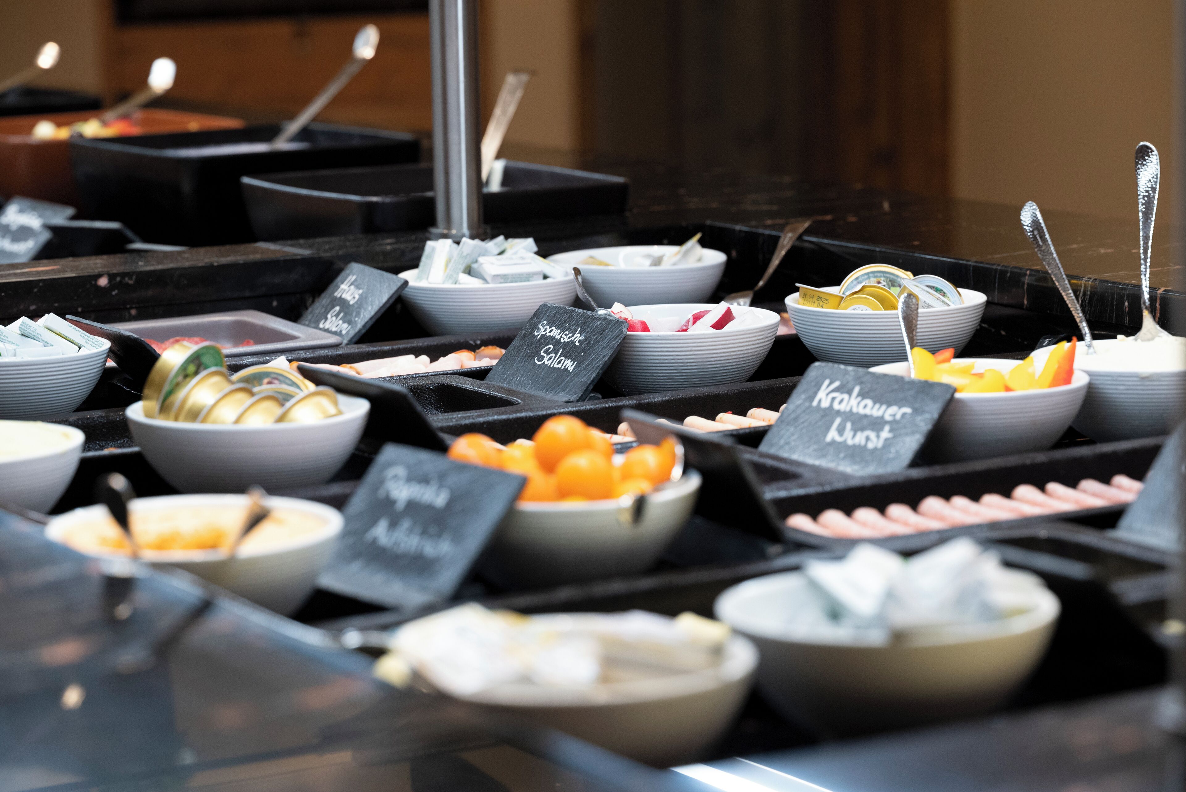 A buffet with various food stations labeled "Spanish Salami," "Nokauer Kuehl," and "Aji Chileno."