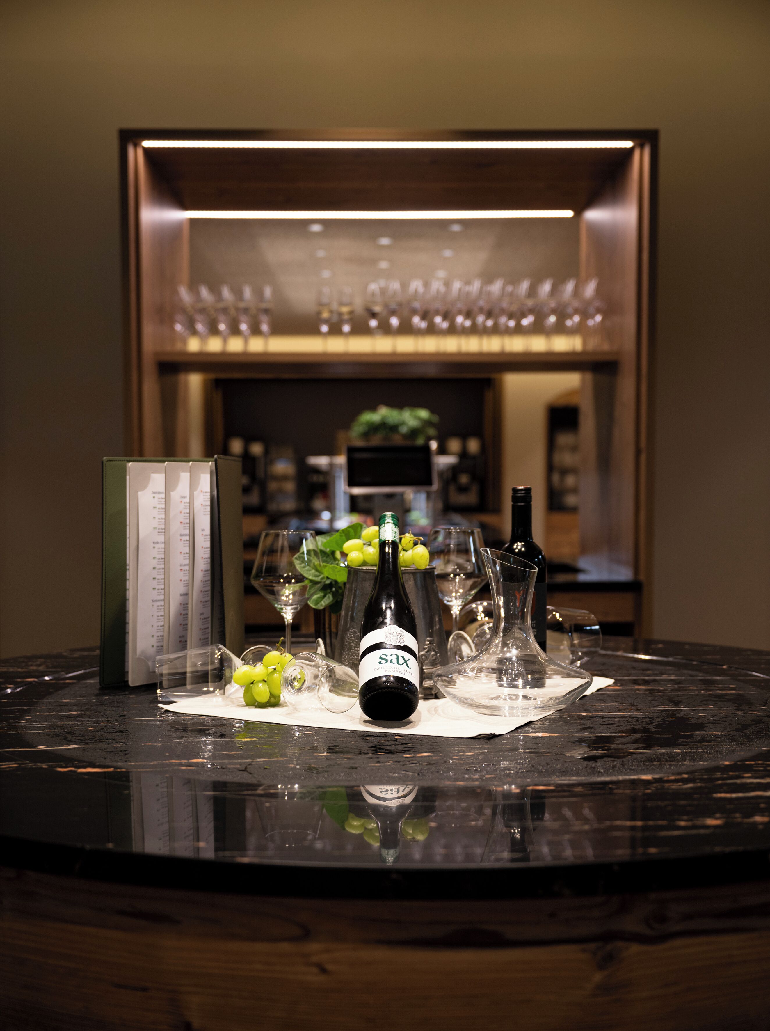 A bar area with a bottle of Sax wine, glasses, and a menu on a marble table.