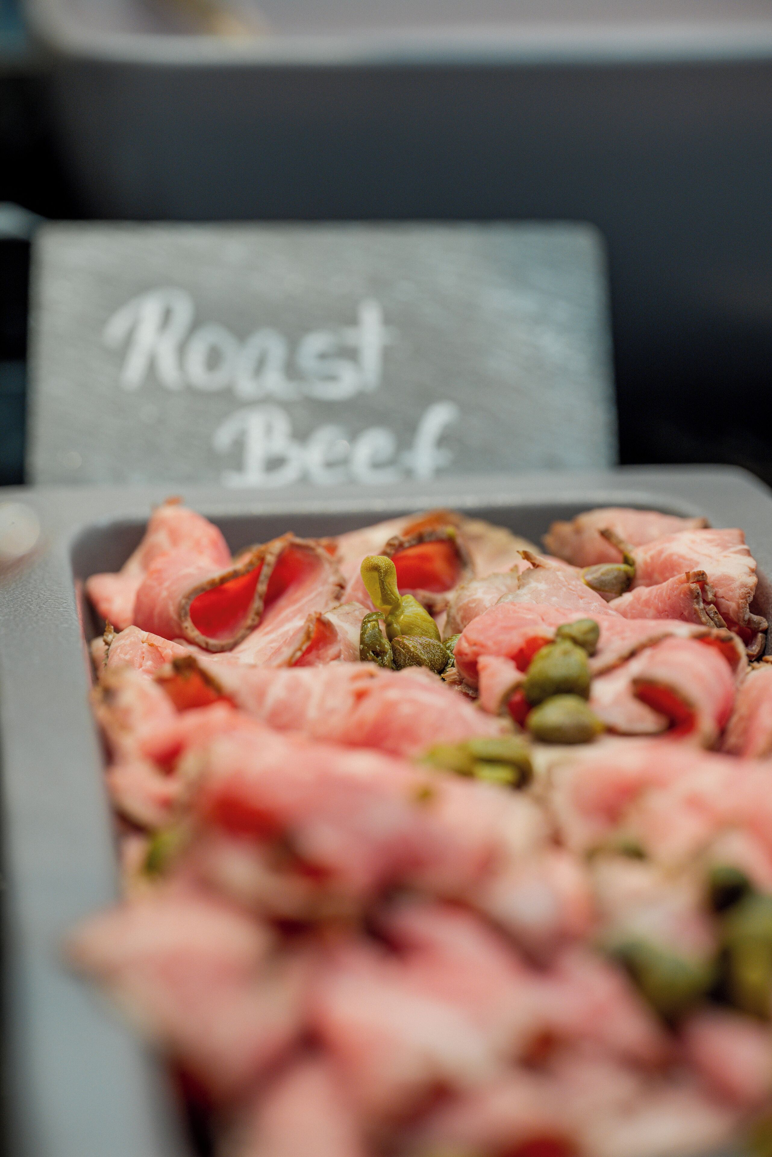 A tray of sliced roast beef with capers and a sign that reads "Roast Beef".