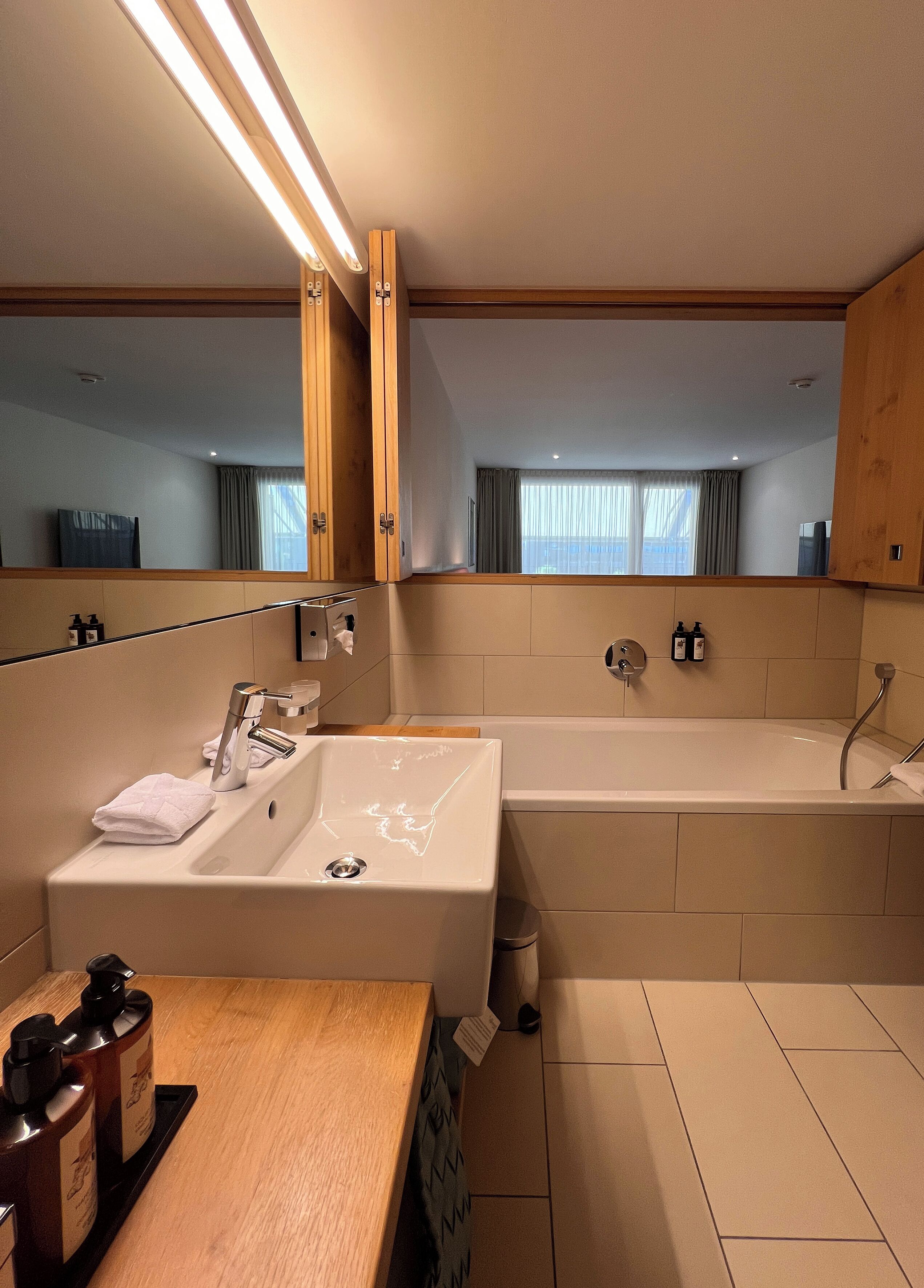 A modern bathroom with a large mirror, a sink, a bathtub, and a wooden vanity.