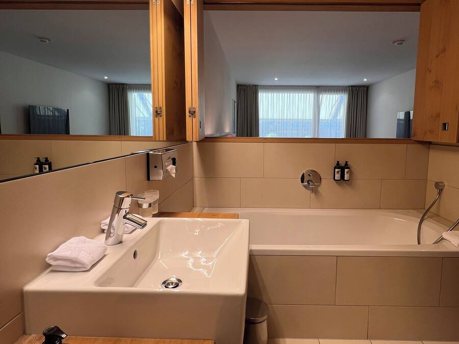 Une salle de bain moderne avec un grand miroir, un lavabo, une baignoire et un meuble-lavabo en bois.