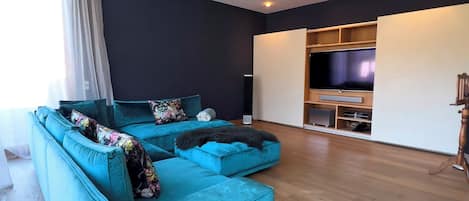 Una sala de estar moderna con un sofá seccional color turquesa, un televisor de pantalla plana y un mueble de entretenimiento de madera.
