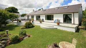 Une maison à deux étages avec une grande véranda à l’avant, des plantes en pot et une pelouse bien entretenue.