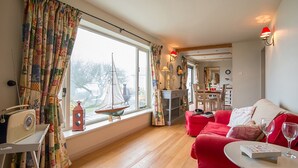 Un salon chaleureux avec un canapé rouge, une petite table sur laquelle se trouvent un livre et un verre, et une fenêtre avec des rideaux.