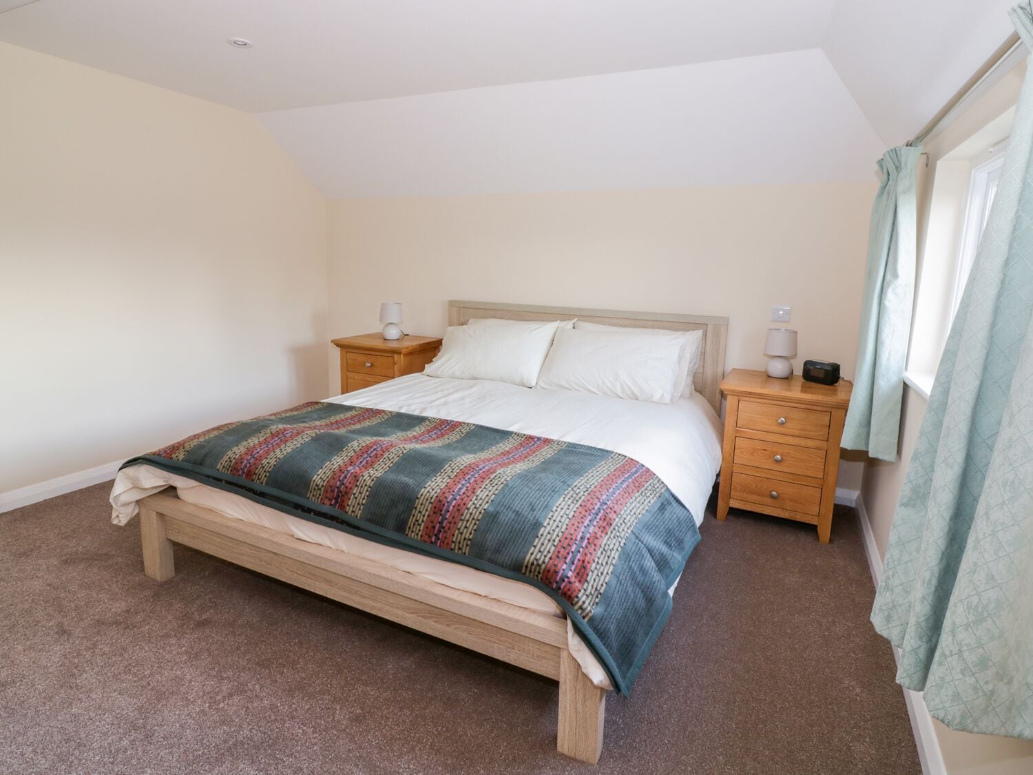 A bedroom with a bed, two bedside tables, and a window with curtains.