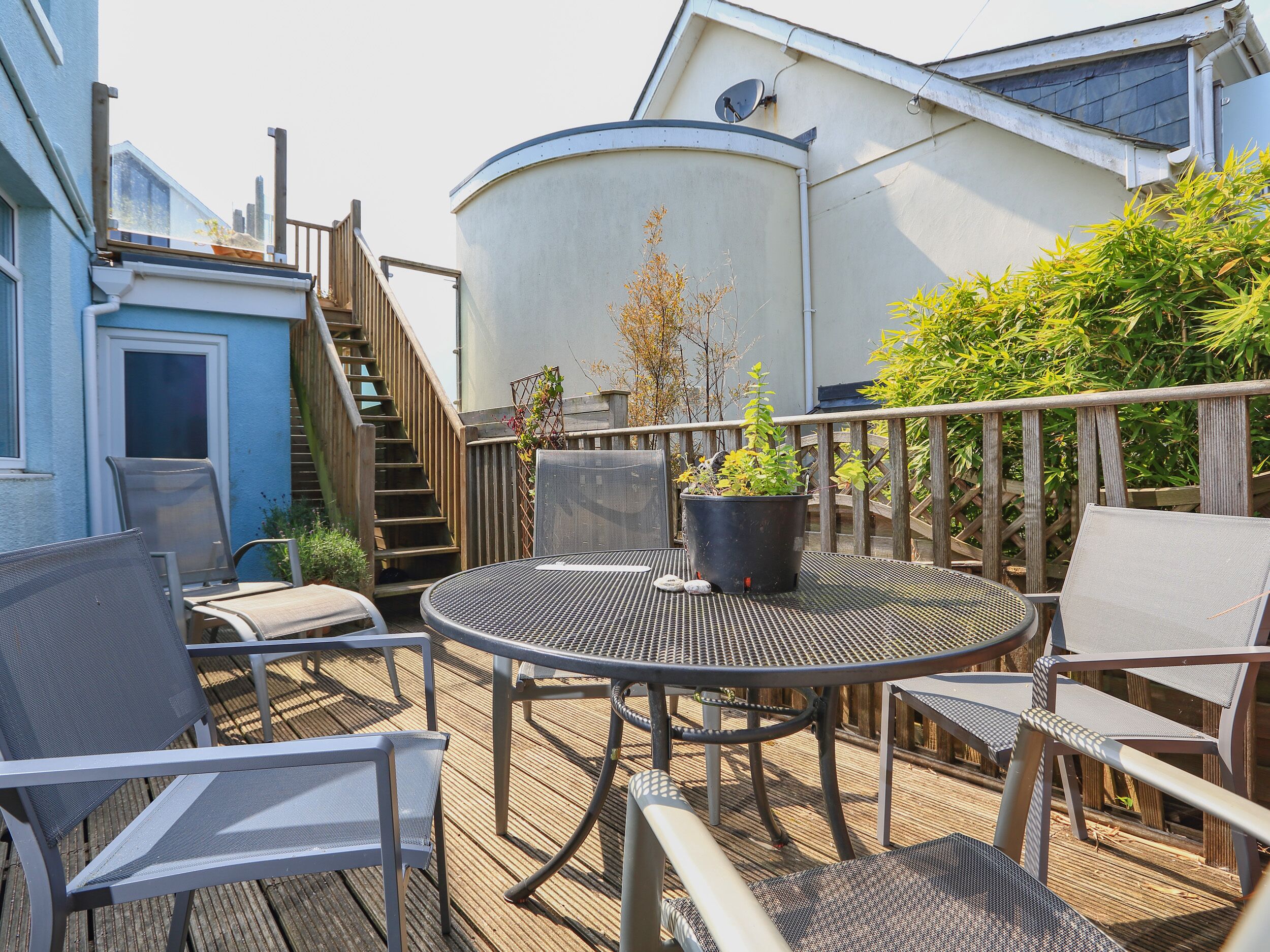 A deck with a round table and chairs, a potted plant, and a staircase leading to a building.
