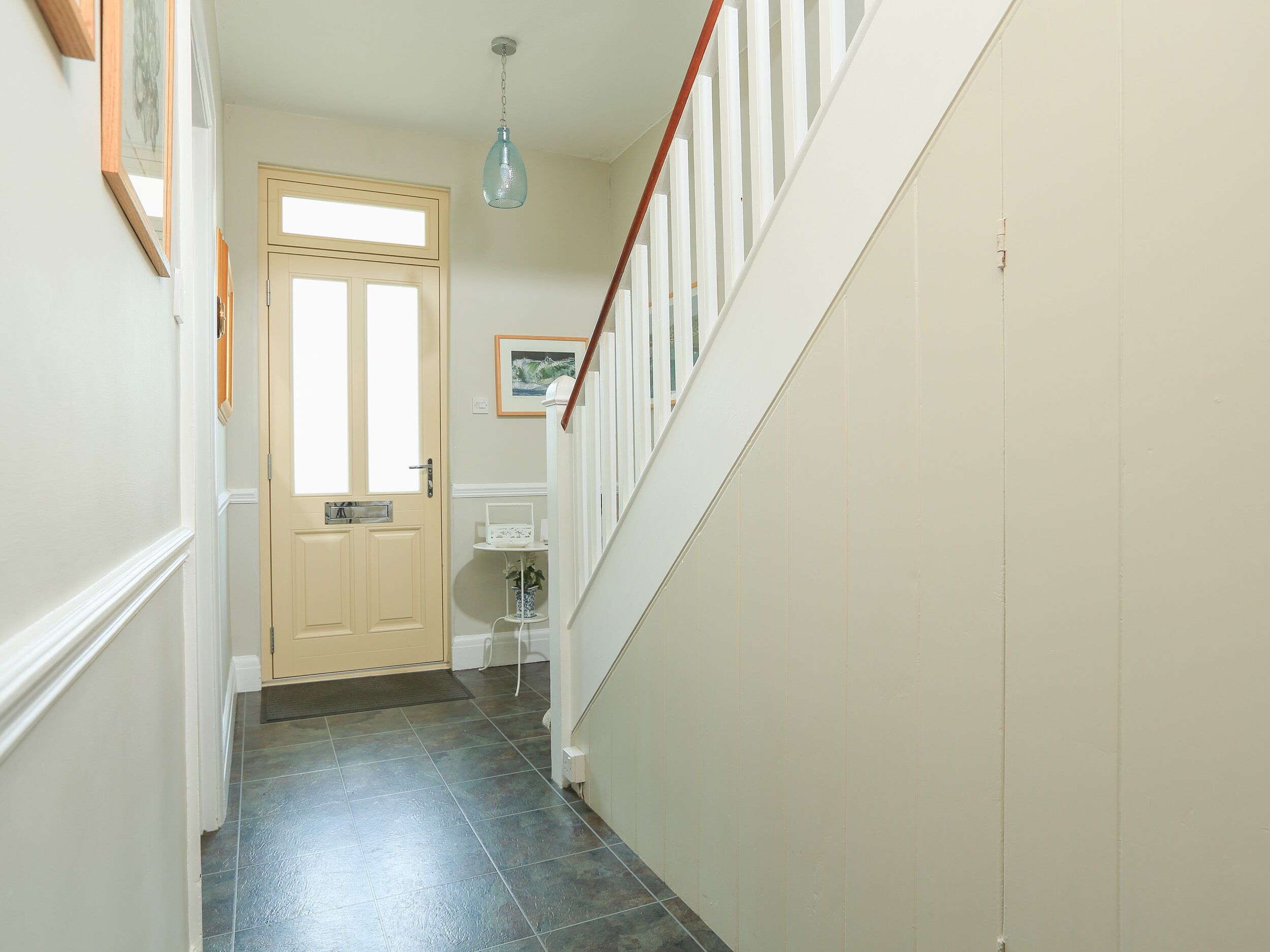 A hallway with a wooden door, a staircase with white railings, and a hanging light fixture.