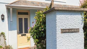 Een huis met een 'Harbourfield' bord, een voordeur en een kleine tuin met planten.