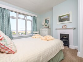 Un dormitorio con cama, cómoda, espejo, chimenea y ventana con cortinas.