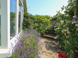 Un jardín con un sendero de piedra, un banco de madera y diversas plantas en flor.
