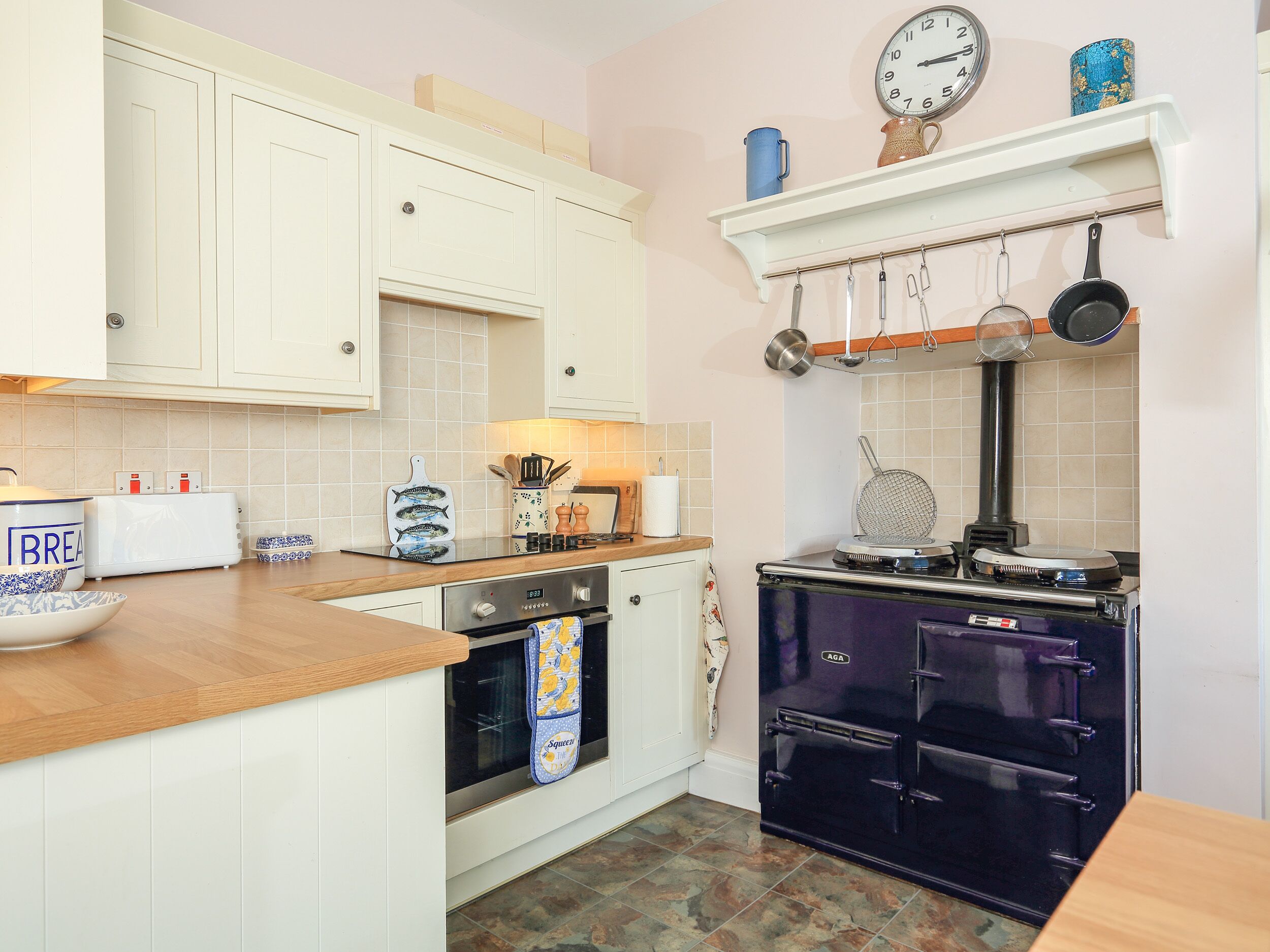 A kitchen with white cabinets, a wooden countertop, a vintage stove, and a clock on the wall.