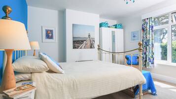 A bedroom with a bed, a nightstand, a lamp, a wardrobe, and a window with curtains.
