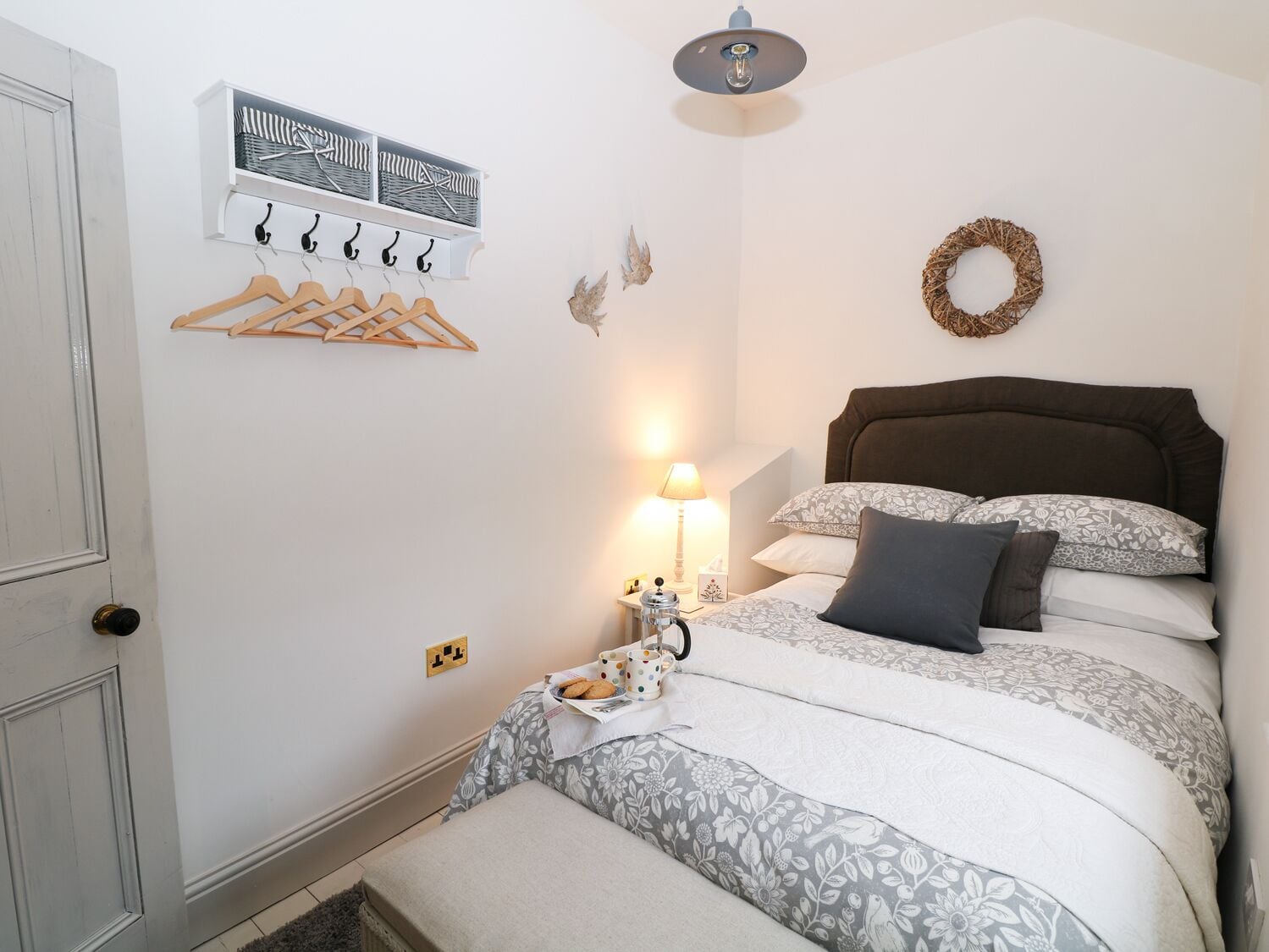 A bedroom with a bed, a wall-mounted coat rack, a wall clock, and a decorative wreath.
