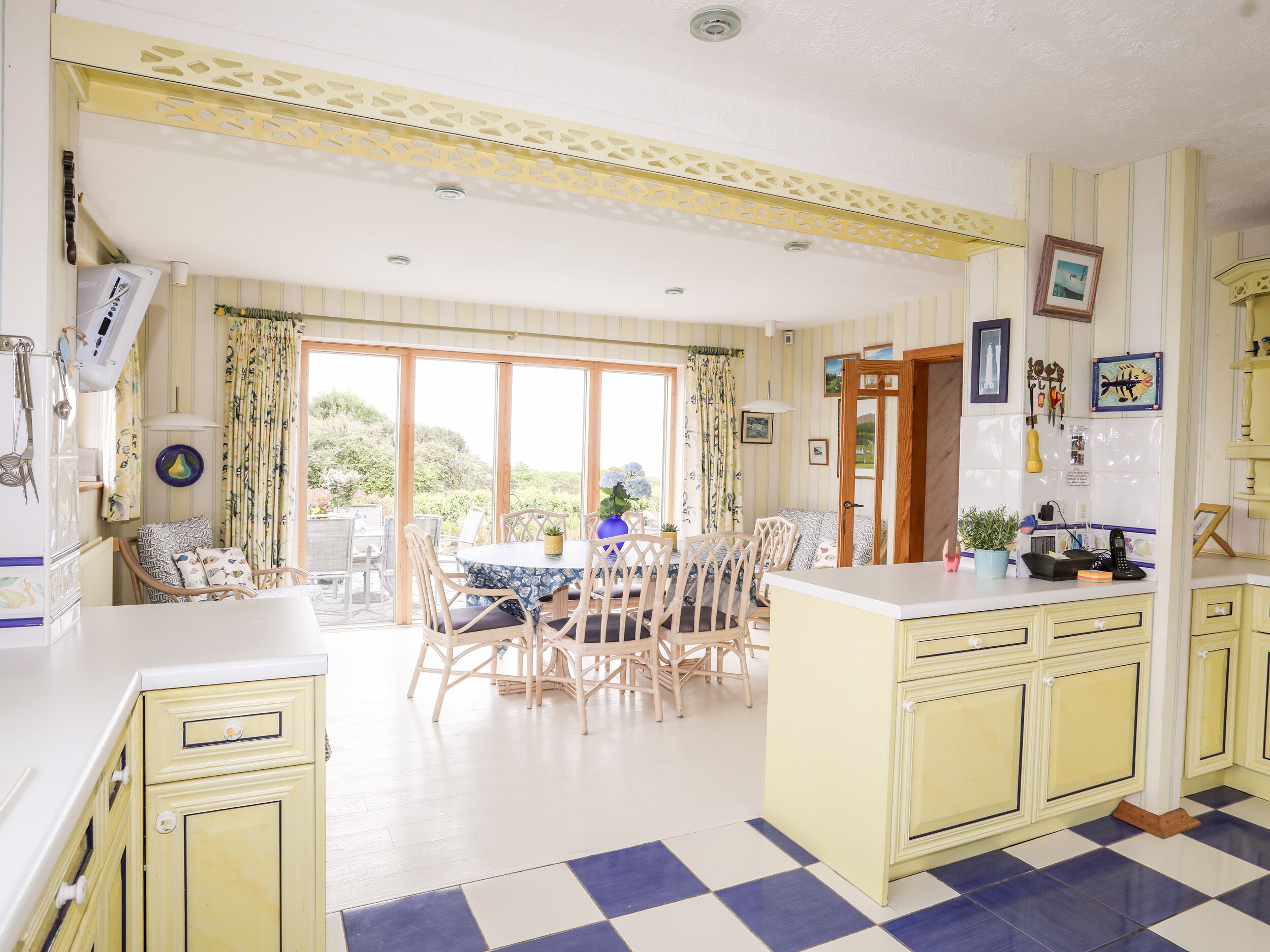 A kitchen with a checkered floor, a dining area with chairs and a table, and a view of greenery outside.