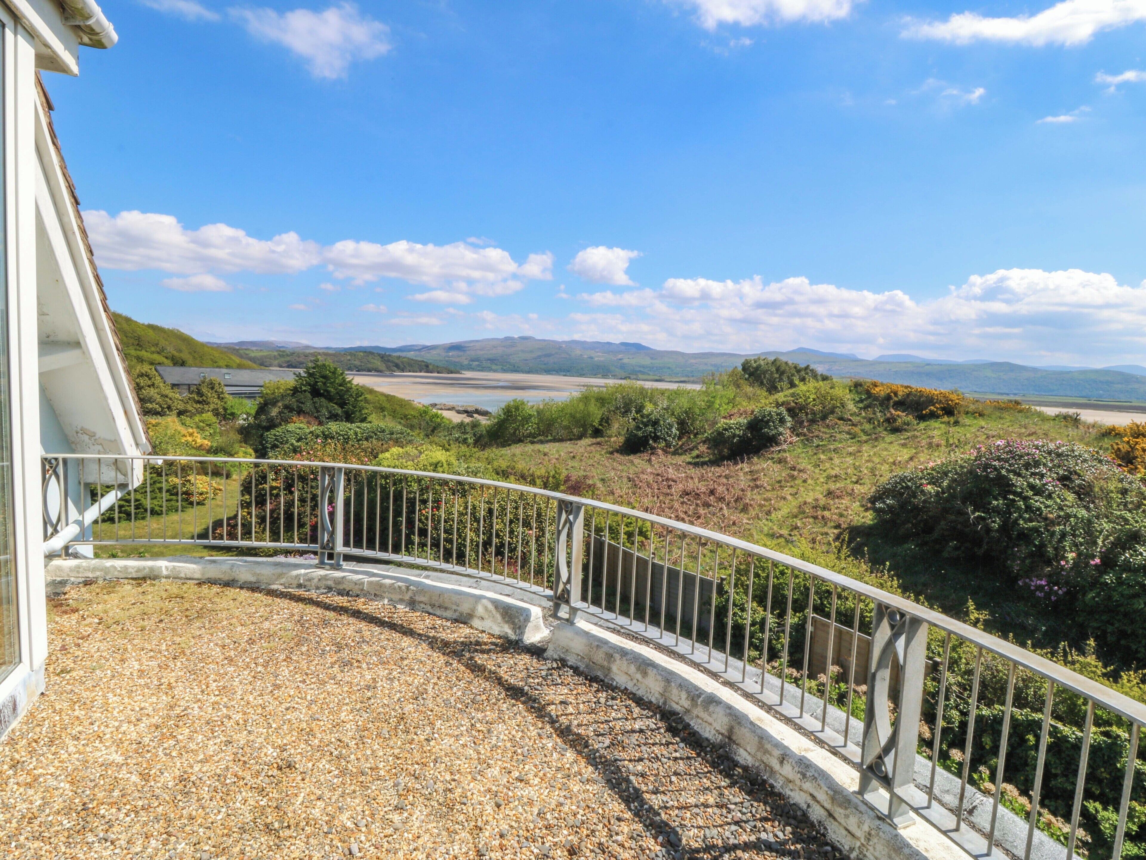 A balcony with a gravel floor, a metal railing, and a view of a coastal landscape with hills and a beach.