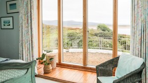 A room with a large window, a wicker chair, a bed, and a potted plant. - Bryn Y Mor, Borth Y Gest (Porthmadog)