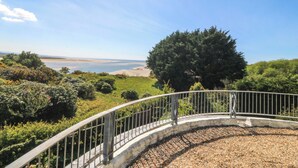 A curved metal railing overlooking a coastal landscape with a large tree and a beach in the distance. - Bryn Y Mor, Borth Y Gest (Porthmadog)
